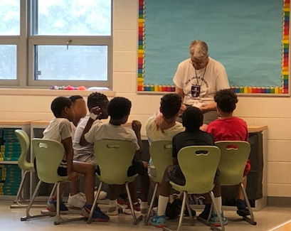 A man with an open Bible share truths with 7 interested boys seated in chairs.