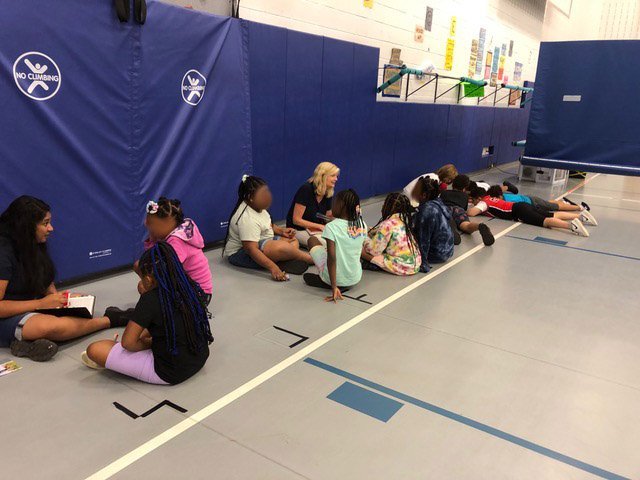 Three groups of children who indicated they want to believe in Jesus sit along the wall of a gym; an adult is meeting with each group, answering questions and teaching about Jesus.