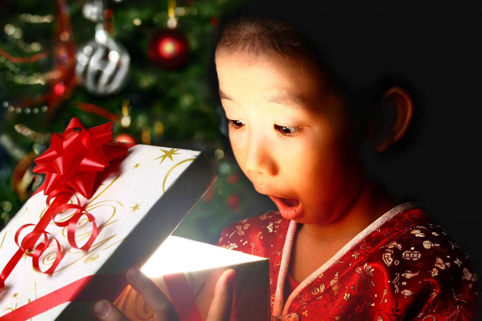 Child stares in wonder into a partially opened Christmas package. A soft glow comes from inside the box.